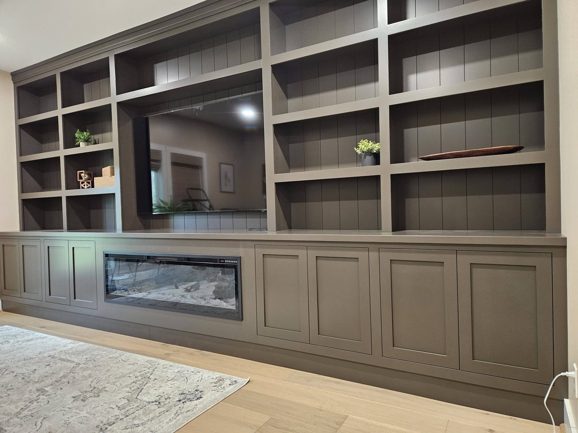A floor-to-ceiling built-in media wall in painted gray-brown, with open display shelving and a long linear fireplace across the base cabinets