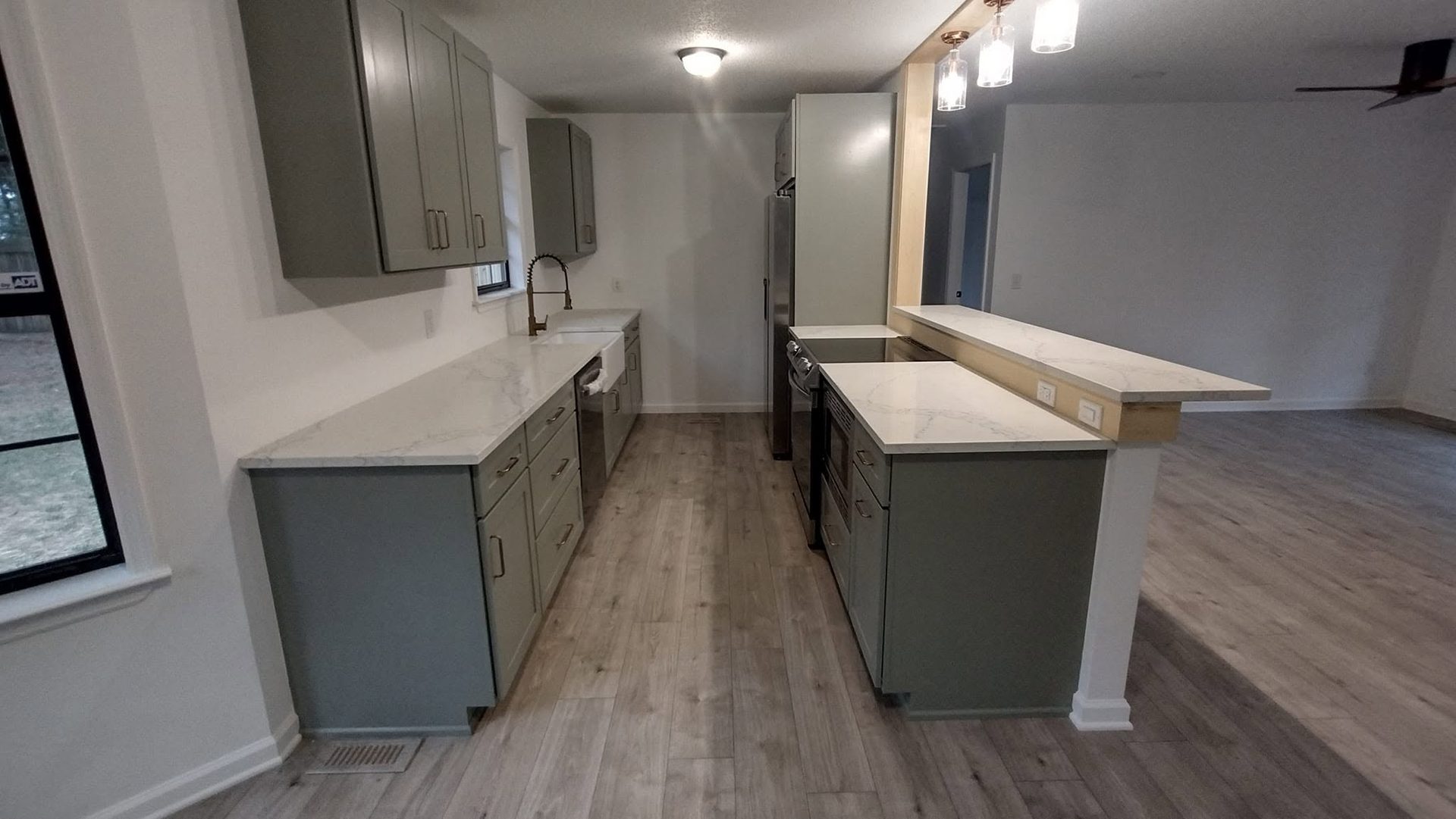 Full custom kitchen with gray-green shaker base cabinets, white countertops, and an island opening onto the living space