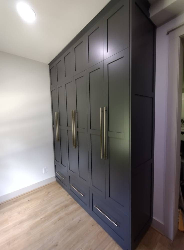 Tall floor-to-ceiling wardrobe cabinets in gray shaker doors with long brass bar pulls