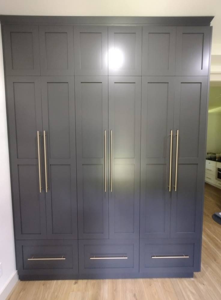 A bank of tall gray shaker cabinets with vertical brass bar pulls
